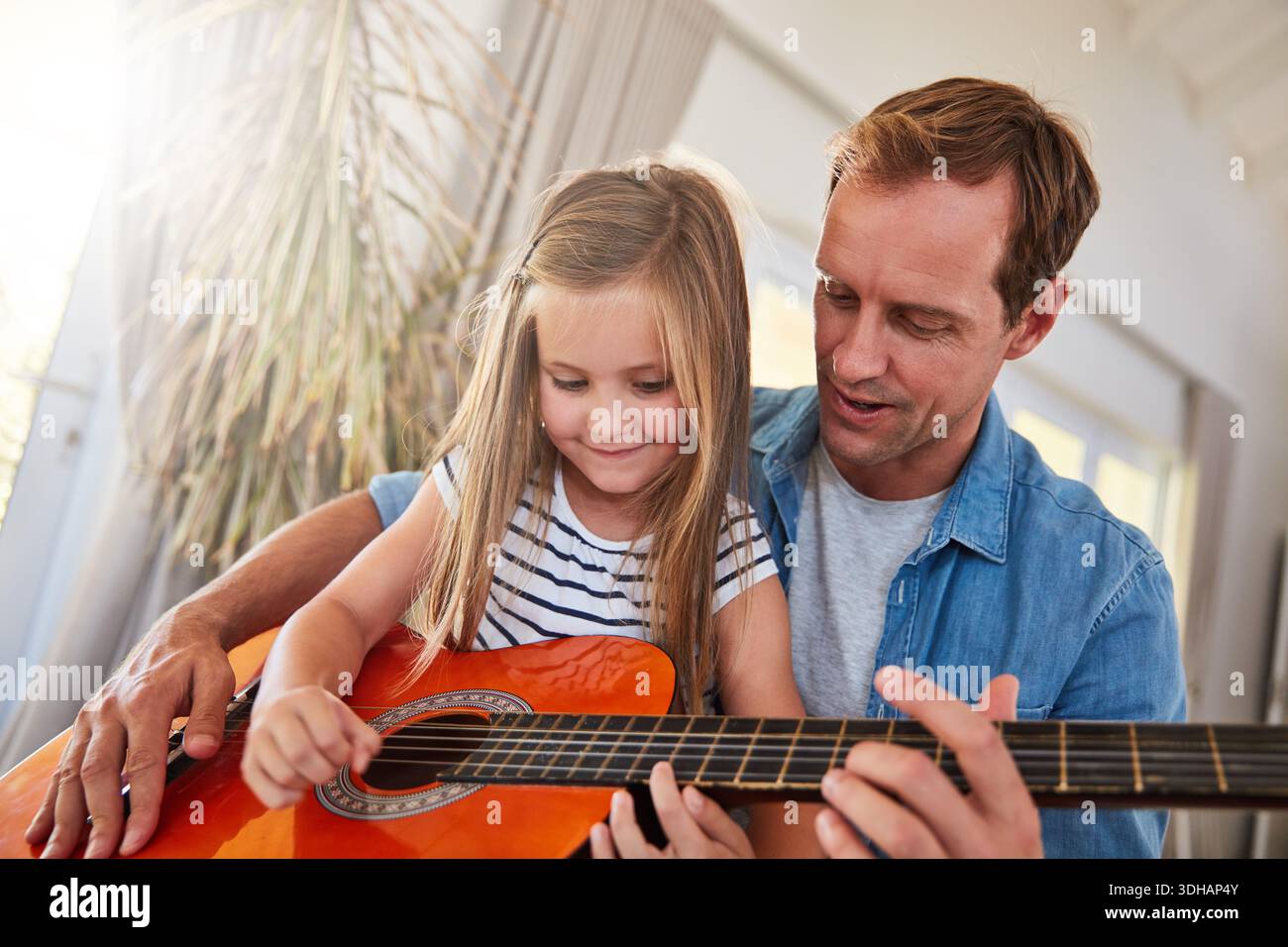 Chitarra, musica e apprendimento con il padre, la ragazza e il legame nel salotto di casa. Strumento, amore e sorriso con genitori, figli e insegnanti Foto Stock