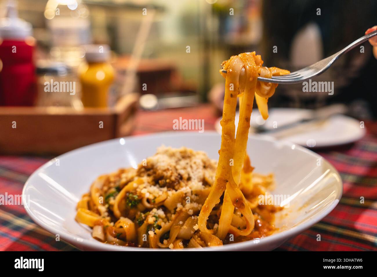 Tagliatelle cotte con sollevamento forche servite con salsa salata di carne e formaggio in piatto bianco su tovaglia di tartan Foto Stock