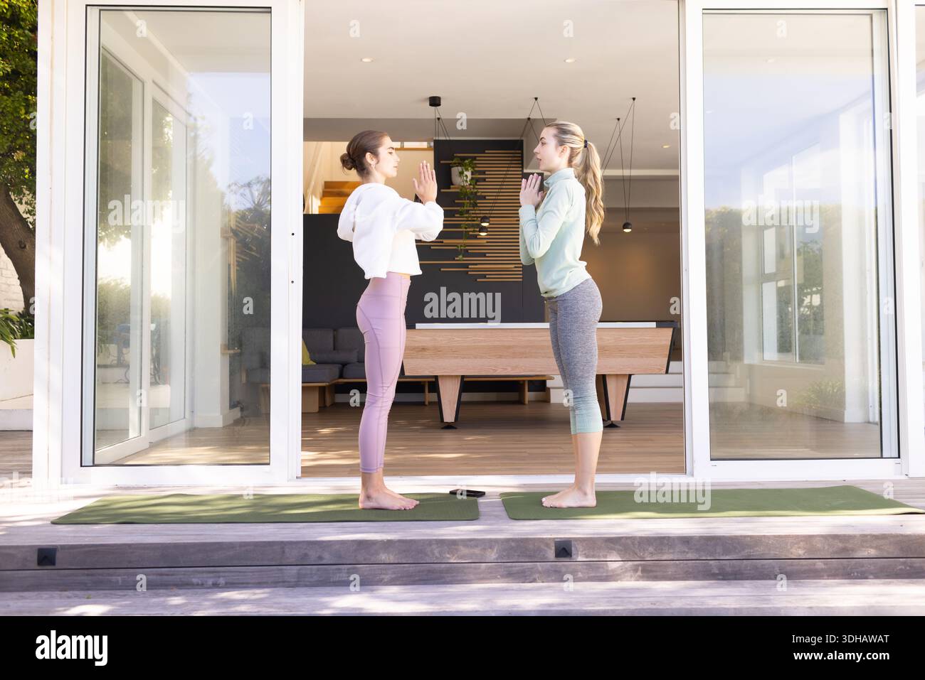 Amici femminili in piedi sul ponte con abiti da yoga che tengono posa di preghiera su tappeti verdi con lo smartphone Foto Stock