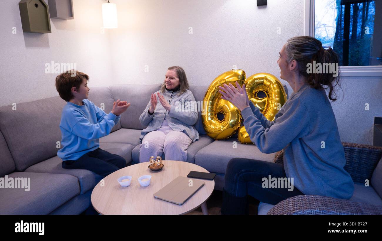 Tre generazioni di familiari che battono le mani e celebrano un buon compleanno a casa Foto Stock
