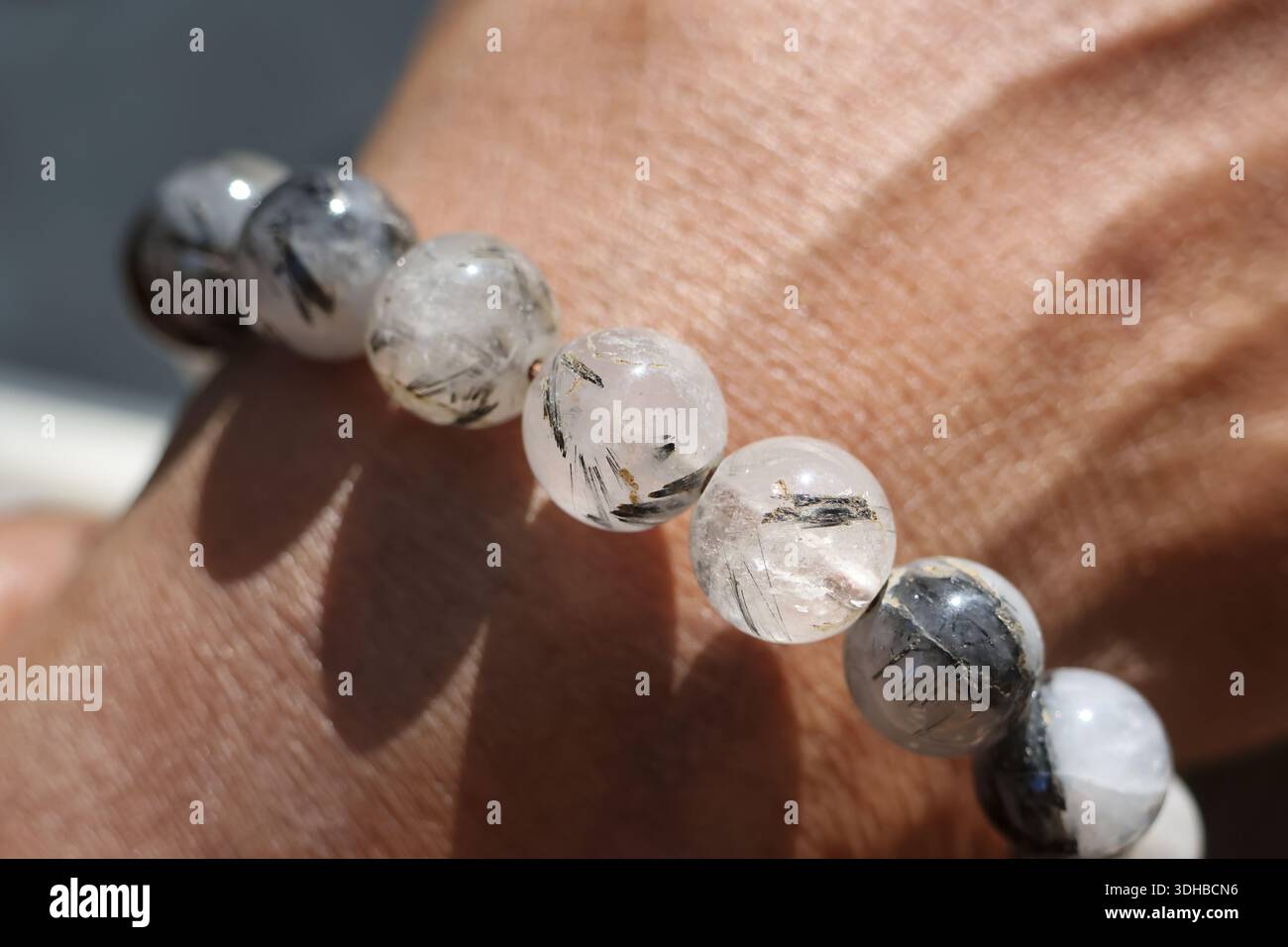 Primo piano del braccialetto spirituale in pietra di quarzo nero rutilato polso maschile che mostra la consistenza e il dettaglio di perle di pietre preziose minerali per la guarigione dell'energia e la fortuna Foto Stock