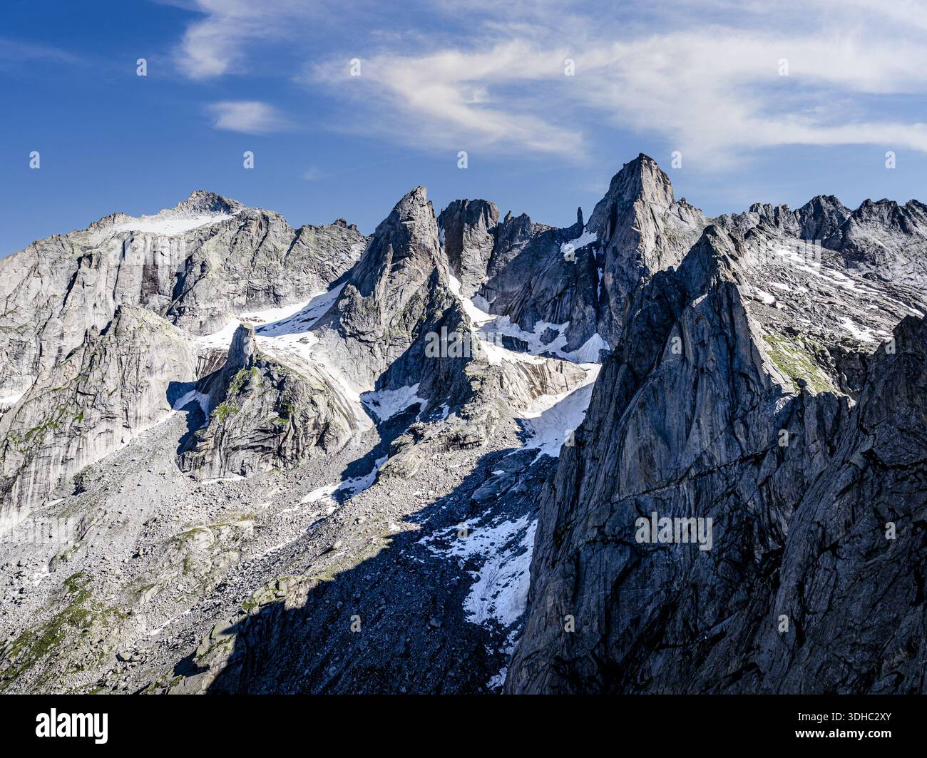 Veduta aerea delle aspre cime rocciose che perforano il cielo, le loro facce innevate contrastano con il blu profondo sopra, Valmasino, Lombardia, Italia. Foto Stock