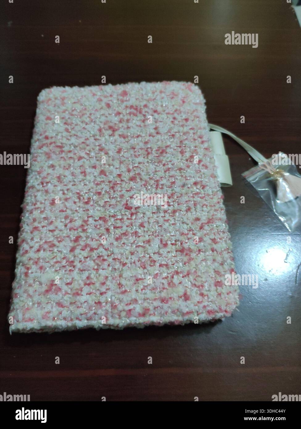 Copertura per notebook in tweed bianco e rosa testurizzato su una superficie in legno Foto Stock