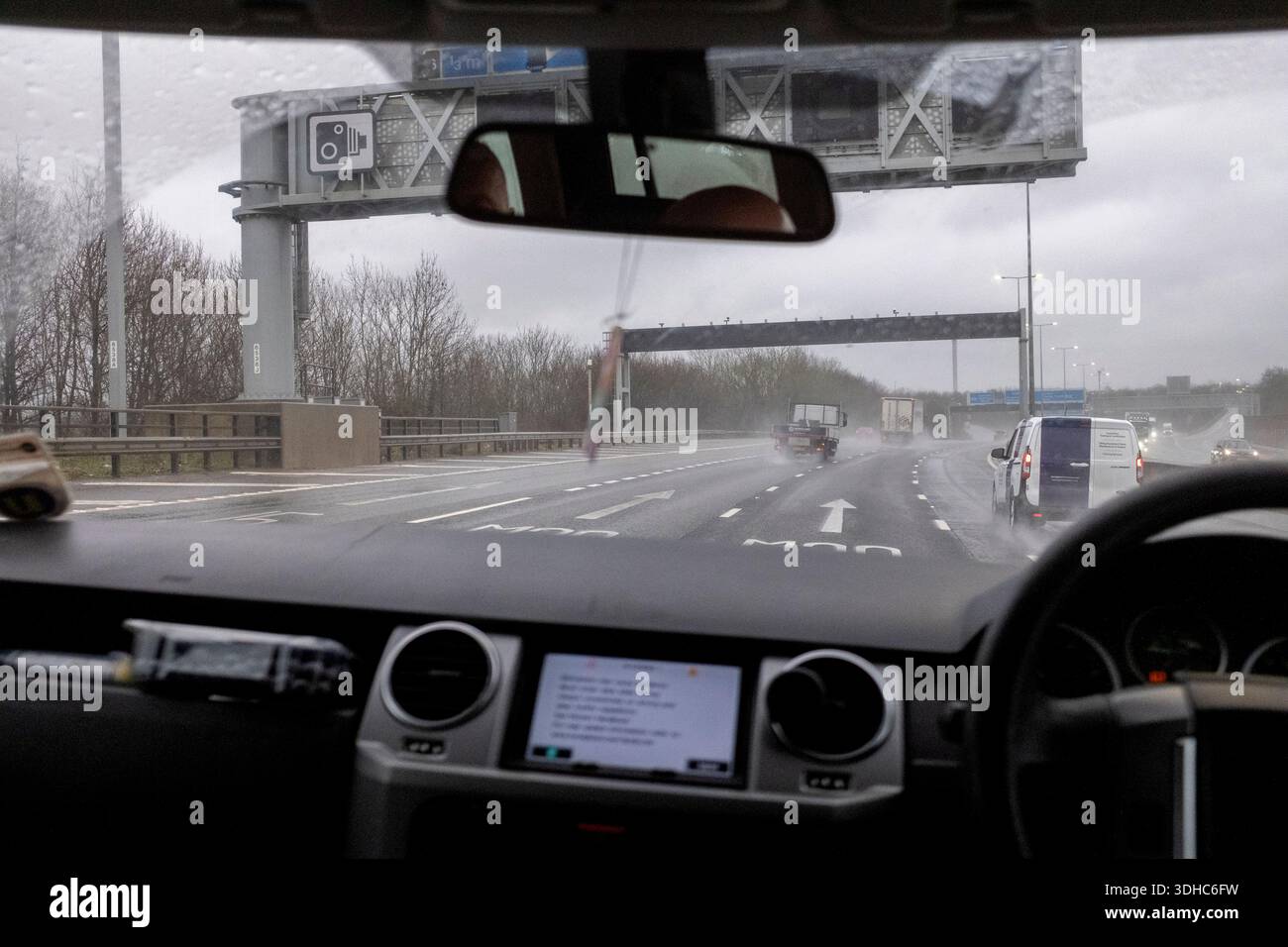 Vista interna da un Land Rover Discovery con guida a destra, in viaggio su un'autostrada britannica a più corsie, tempo piovoso, segnaletica sopraelevata e auto in vista Foto Stock