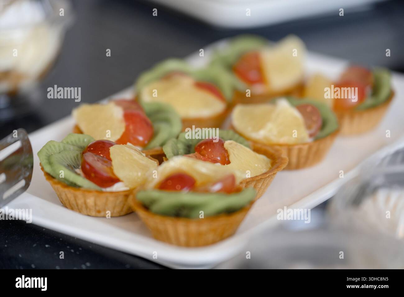 Tortine dolci con kiwi, uva e panna d'arancia. Mini cesti da dessert con frutta e zucchero a velo preparati per un banchetto festivo Foto Stock