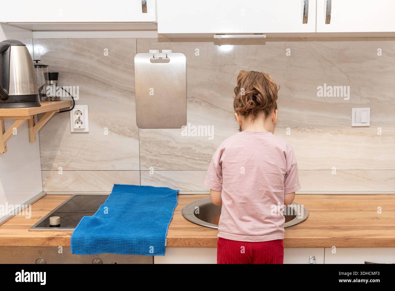 Una bambina adorabile che lava i giocattoli di plastica, frutta e verdura nel lavandino della cucina Foto Stock
