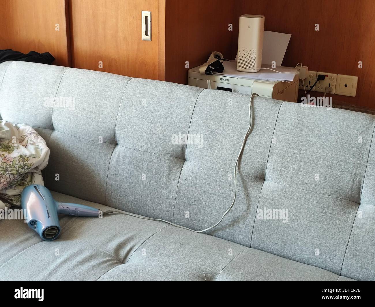 Divano tufted grigio chiaro con asciugacapelli e cavi in un ambiente interno accogliente Foto Stock