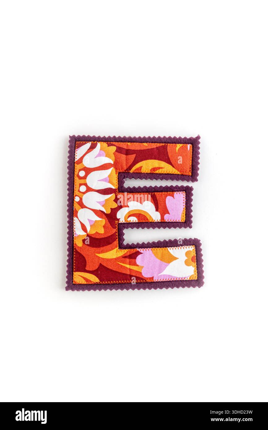 Fotografia ravvicinata di una lettera e in tessuto decorativo realizzata in tessuto colorato con bordi cuciti. Colori vivaci, design floreale e ha Foto Stock
