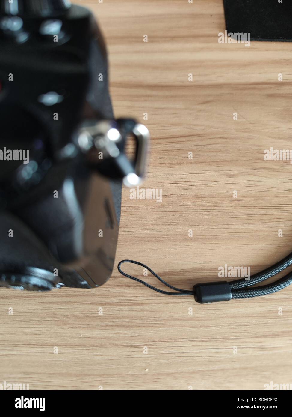 Primo piano di una fotocamera DSLR con cinturino da polso su una superficie in legno Foto Stock