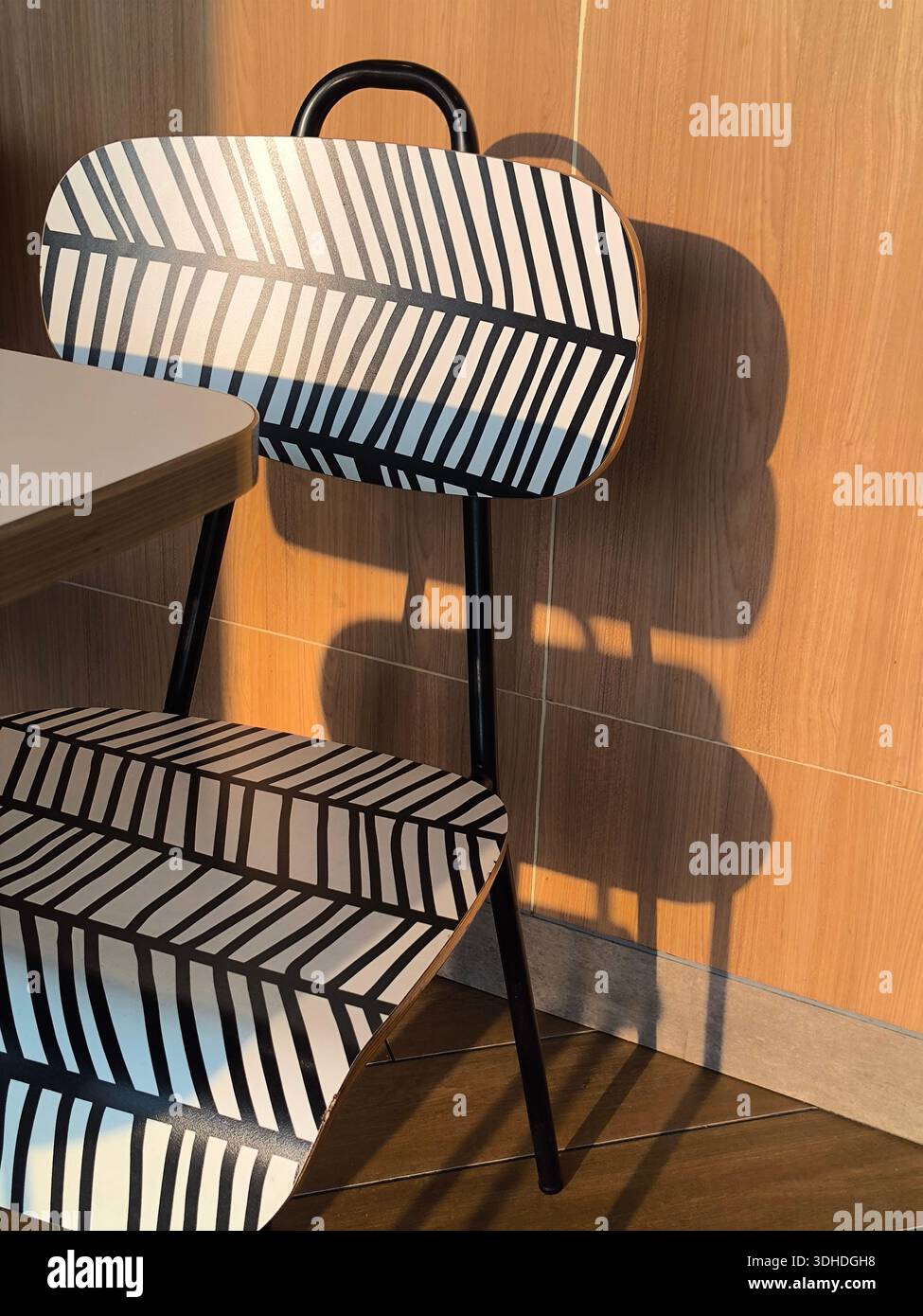 Moderna sedia a righe con audace motivo geometrico che getta ombra contro le pareti in legno Foto Stock