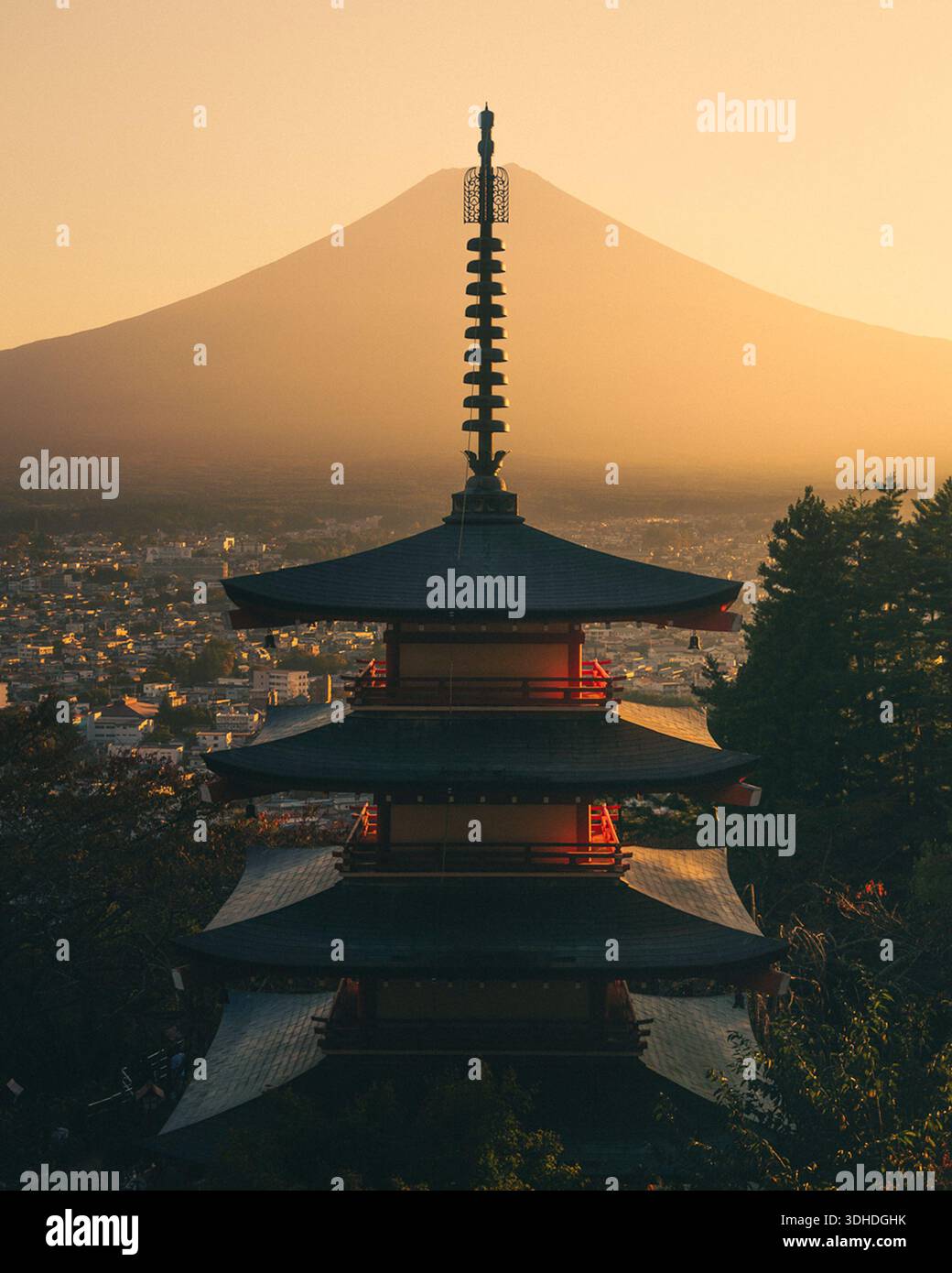 Vista dei livelli vermillion della Pagoda di Chureito che contrastano con il soffice bagliore dorato del Monte Fuji, con il paesaggio urbano nascosto sotto, Fujikawaguch Foto Stock