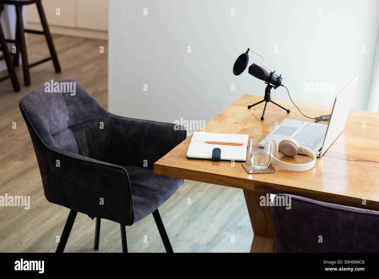La scrivania in legno ospita l'installazione di uno studio domestico con microfono per computer portatile su treppiede, cuffie, notebook, vetro Foto Stock