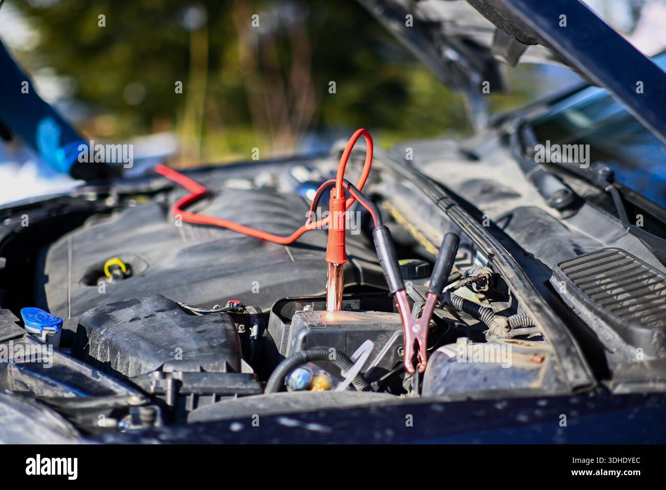 Persona che avvia la batteria di un'auto con dei ponticelli e apre il cofano. Foto Stock