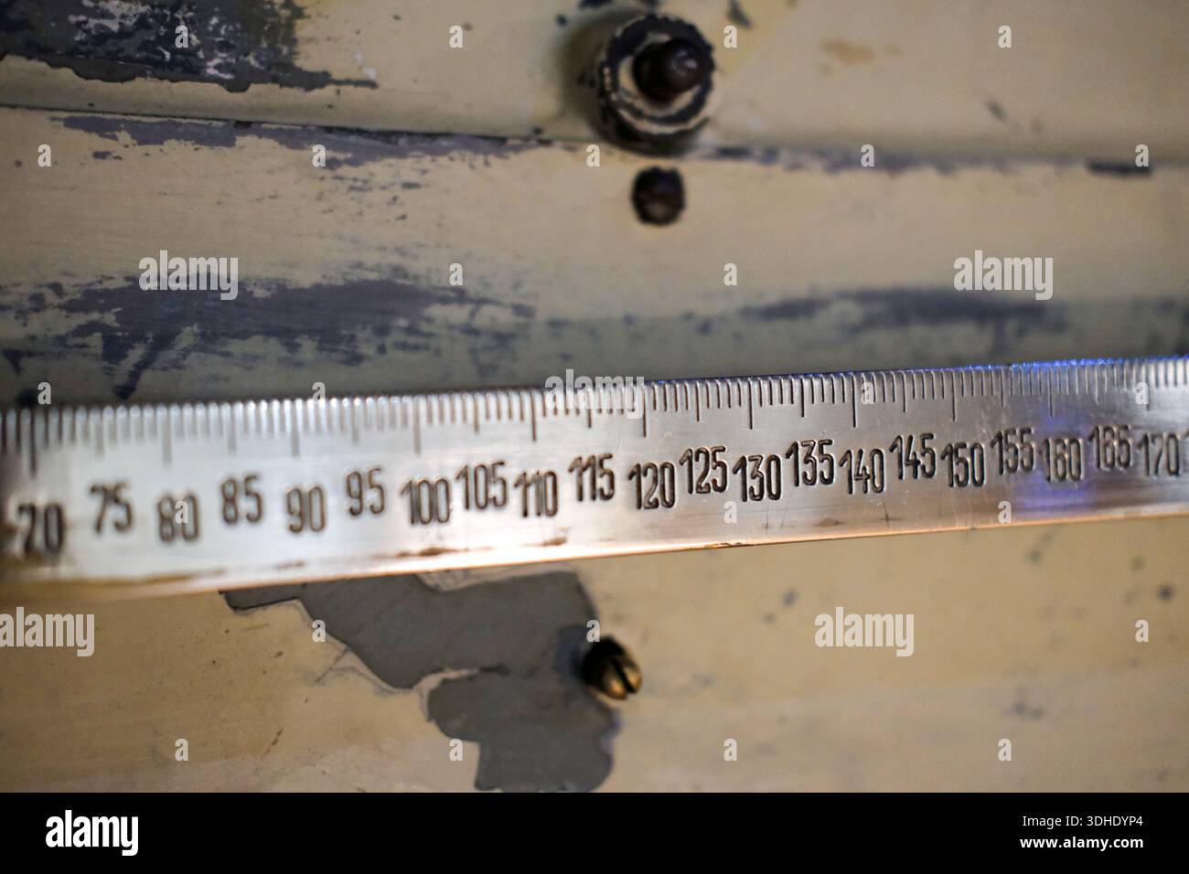 Primo piano del righello di misurazione in argento con numeri incisi e segni di spunta, fissato a uno sfondo metallico verniciato usurato con viti visibili Foto Stock