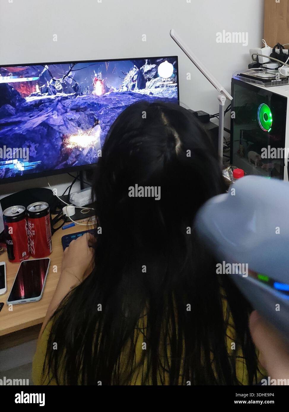 Persona che si asciuga i capelli durante il gioco su un ampio monitor Foto Stock