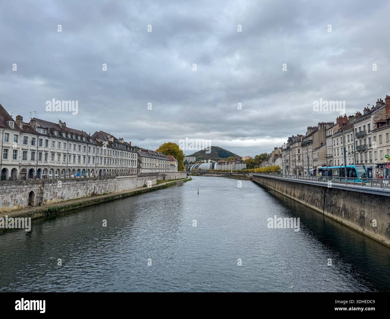 ampia vista del fiume doubs che scorre attraverso la storica città di besanc, in francia. argini in pietra, edifici tradizionali e la collina della cittadella - Immagine stock catturata con smartphone