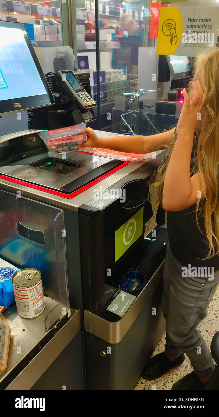 Un'immagine sincera, in stile documentario, di un bambino che impara le proprie abilità di vita utilizzando un sistema di self-checkout del supermercato. Illustra il tema dell'indipendenza e della modalità Foto Stock