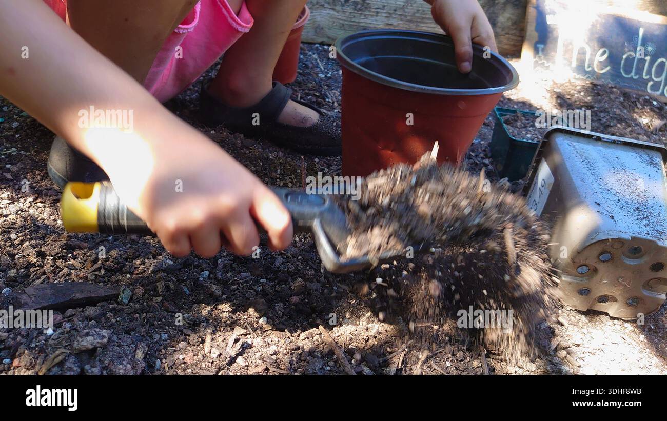 Primo piano delle mani di un bambino con una cazzuola per gettare il terreno in vasi da giardino. Un'immagine concettuale che rappresenta la crescita, la pazienza e il terapeutico Foto Stock