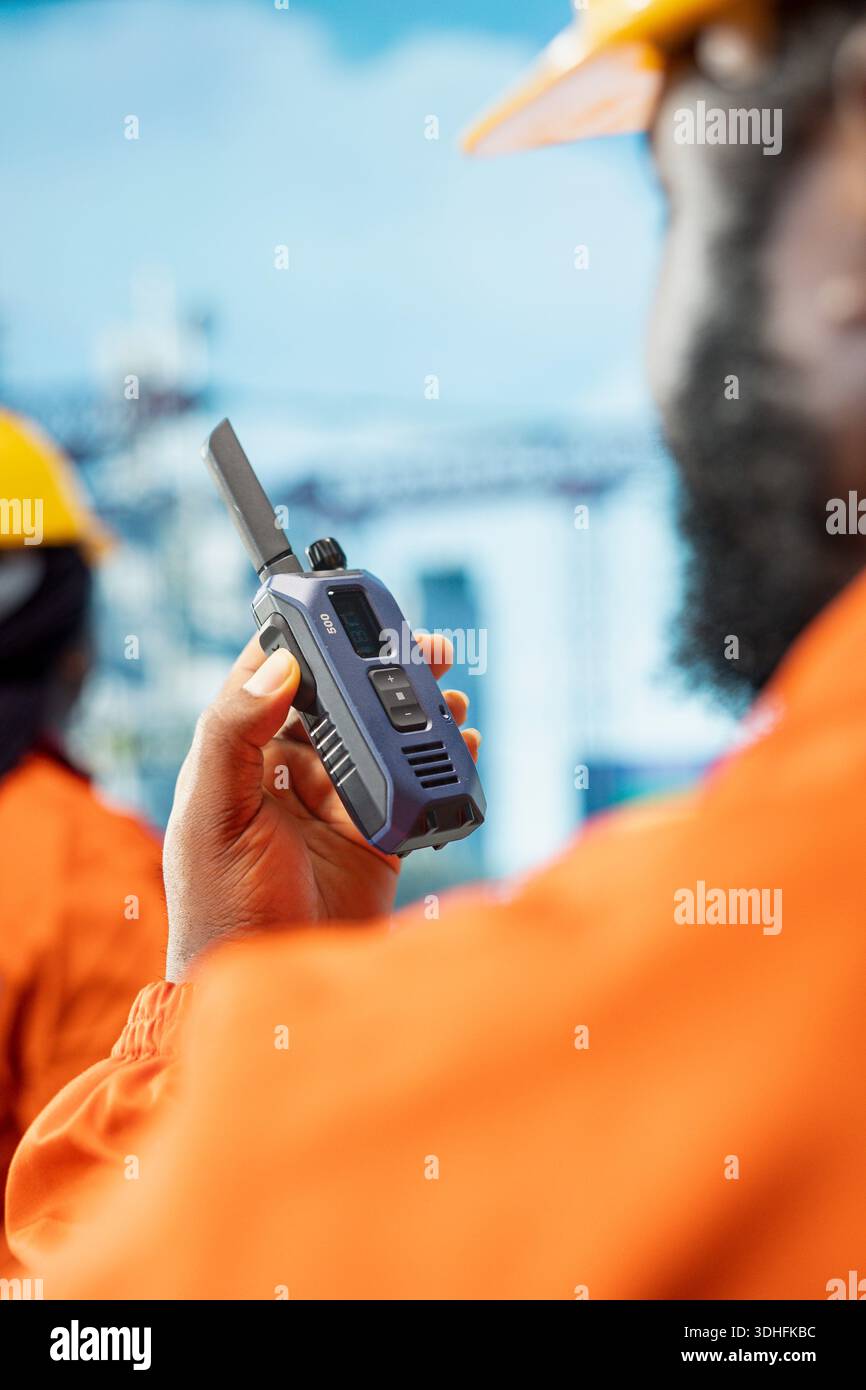 Primo piano di un operaio della piattaforma offshore che parla in walkie talkie, monitorando le operazioni del ponte della piattaforma petrolifera. Operatore radio del carro di perforazione che parla in un dispositivo portatile, rivedendo le operazioni energetiche Foto Stock