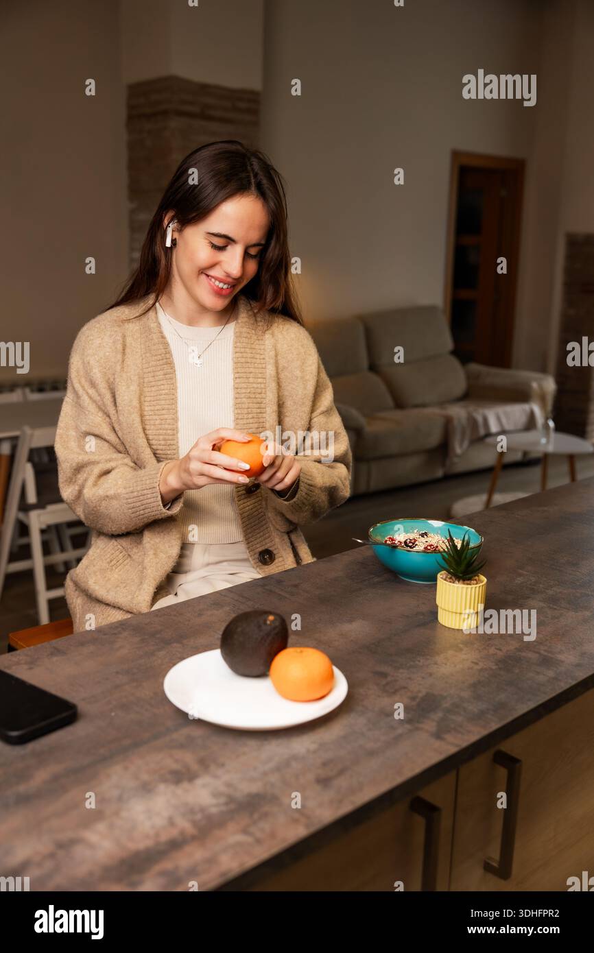 Giovane donna che sbuccia l'arancia per una sana colazione a casa Foto Stock