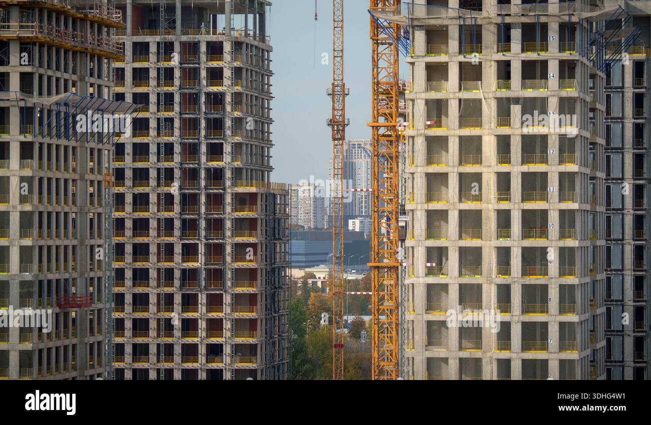Alti edifici residenziali in costruzione con struttura in cemento visibile, ponteggi e gru. Paesaggio urbano visibile attraverso lo spazio tra le torri Foto Stock