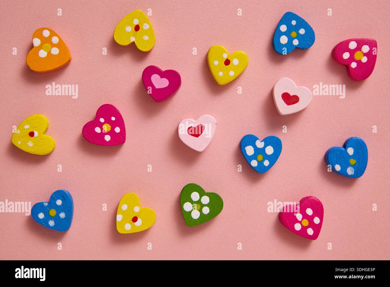 Un piatto di colorate forme a cuore con motivi giocosi e colori luminosi, ordinatamente disposti su un delicato sfondo rosa. Foto Stock