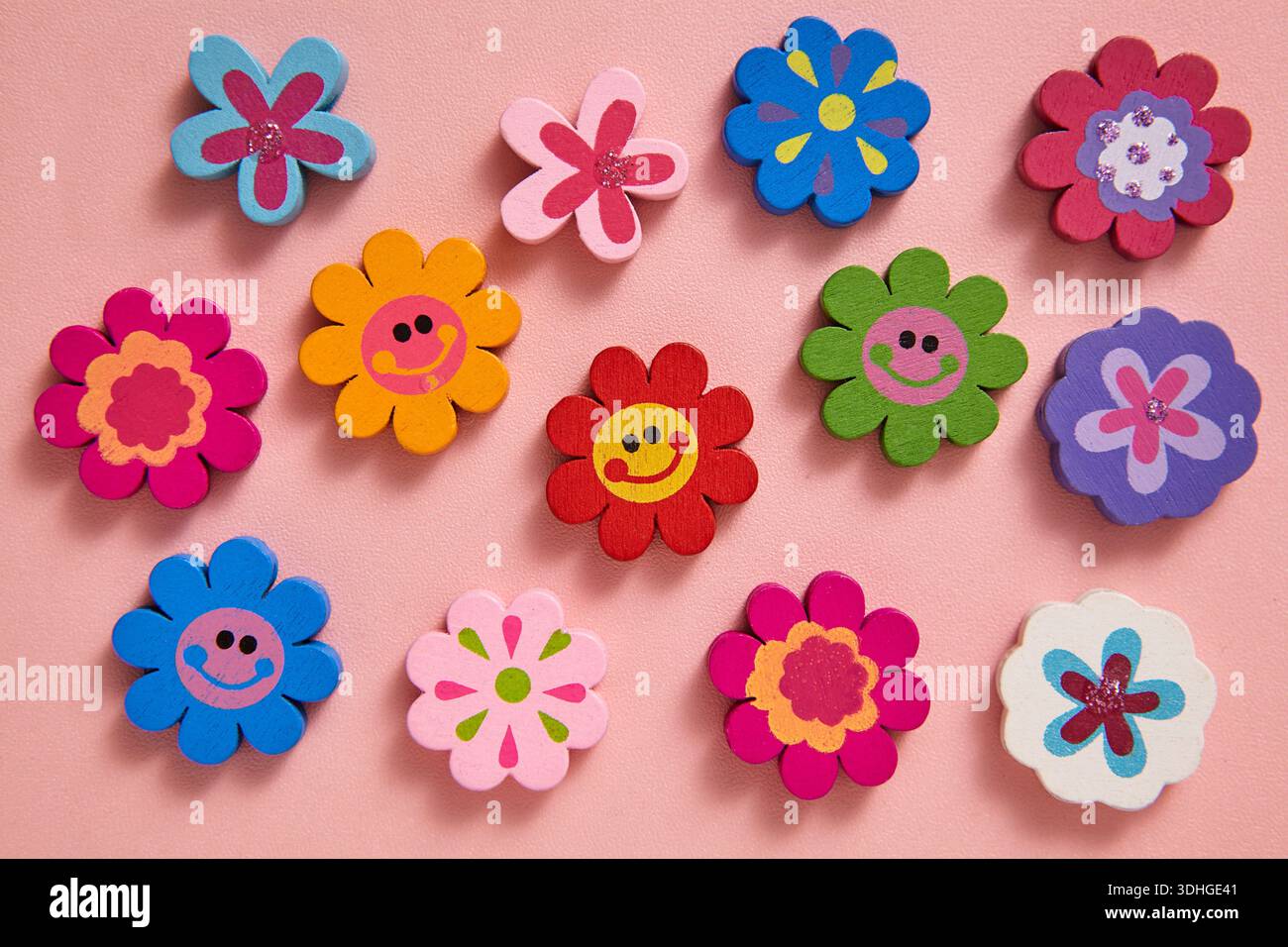 Una vivace e piatta decorazione a forma di fiore con allegri volti sorridenti su uno sfondo rosa tenue. Per biglietti d'auguri allegri Foto Stock