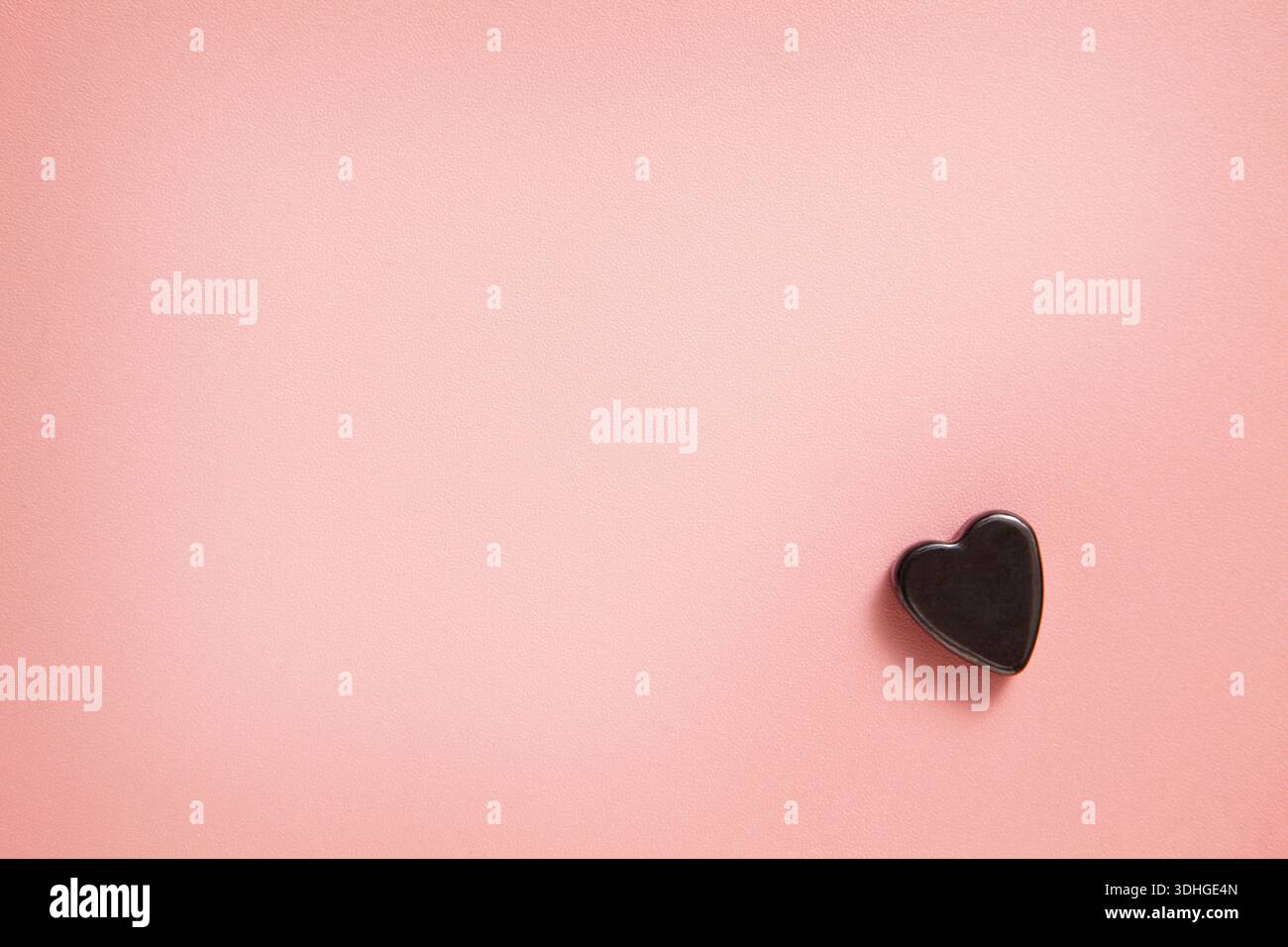 Una composizione minimalista caratterizzata da un piccolo cuore nero posto su un delicato sfondo rosa pastello, che crea una calma e romantica con spazio per le copie. Foto Stock