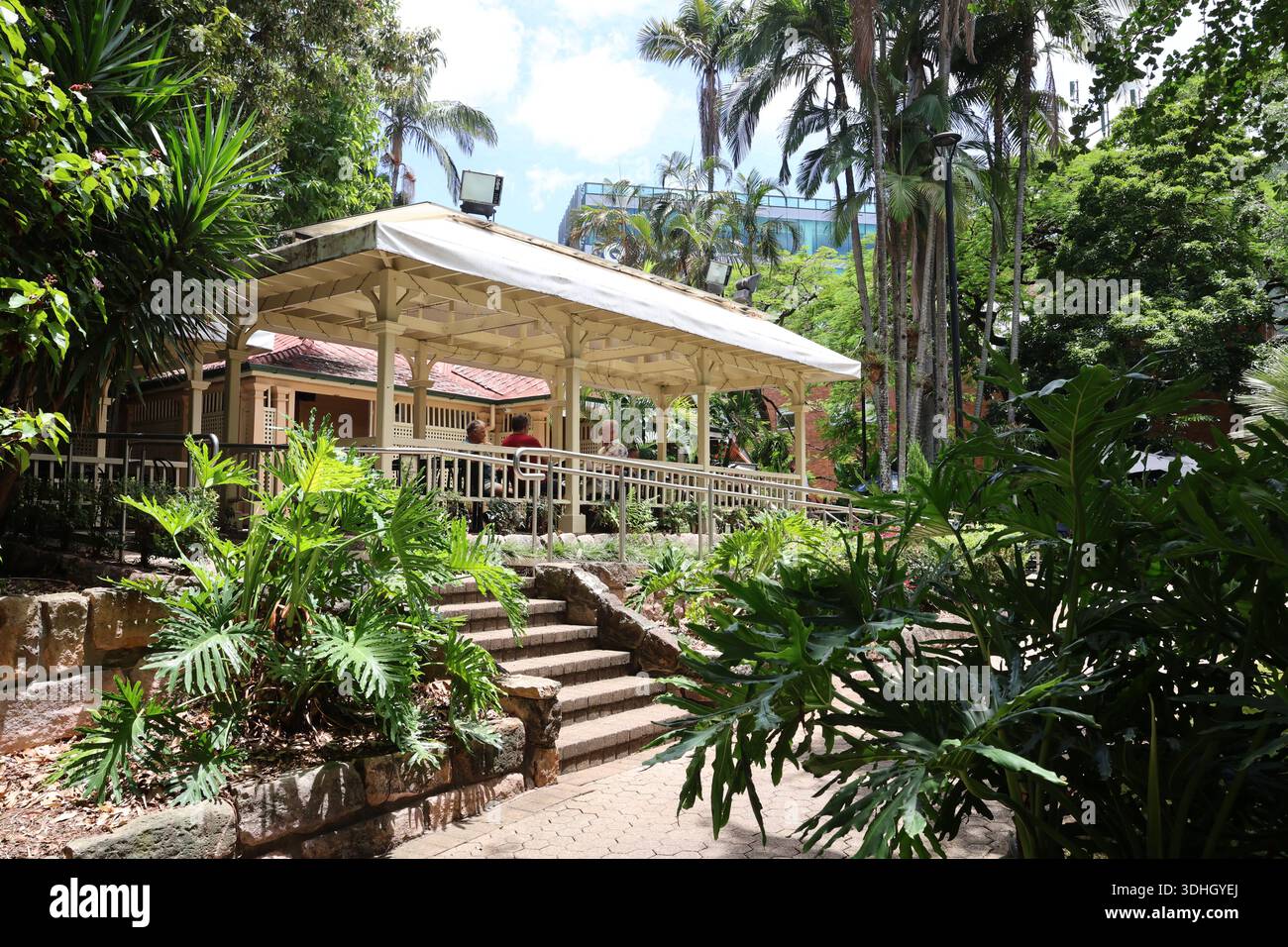 Persone che si rilassano e camminano attraverso i Giardini Botanici di Brisbane con edifici cittadini sullo sfondo, godendo di uno spazio verde in un ambiente urbano. Foto Stock