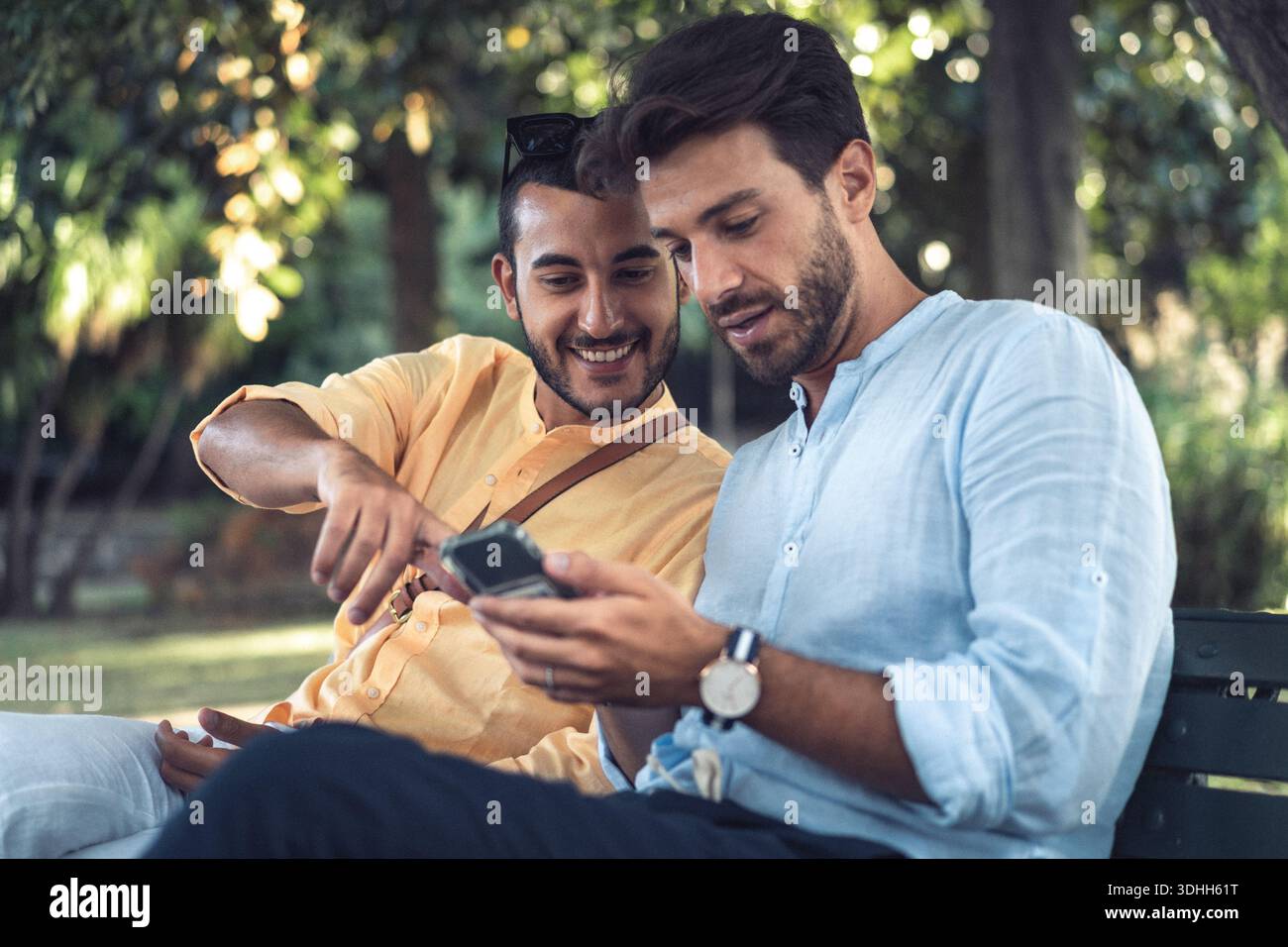Due amici maschi che guardano uno smartphone insieme mentre sono seduti in un parco. Concetto di esperienza digitale condivisa, tecnologia, connessione e tutti i giorni Foto Stock