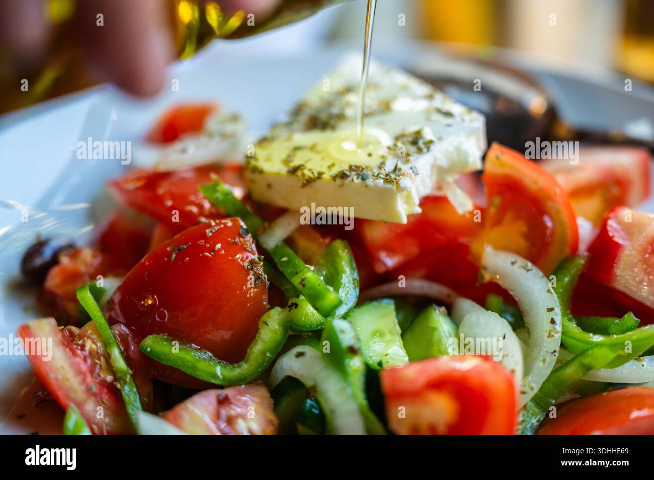 Insalata di verdure tradizionali greche con formaggio e olive, (pomodoro a fette, pepe verde, cipolla), primo piano. L'olio viene versato sul formaggio. Foto Stock