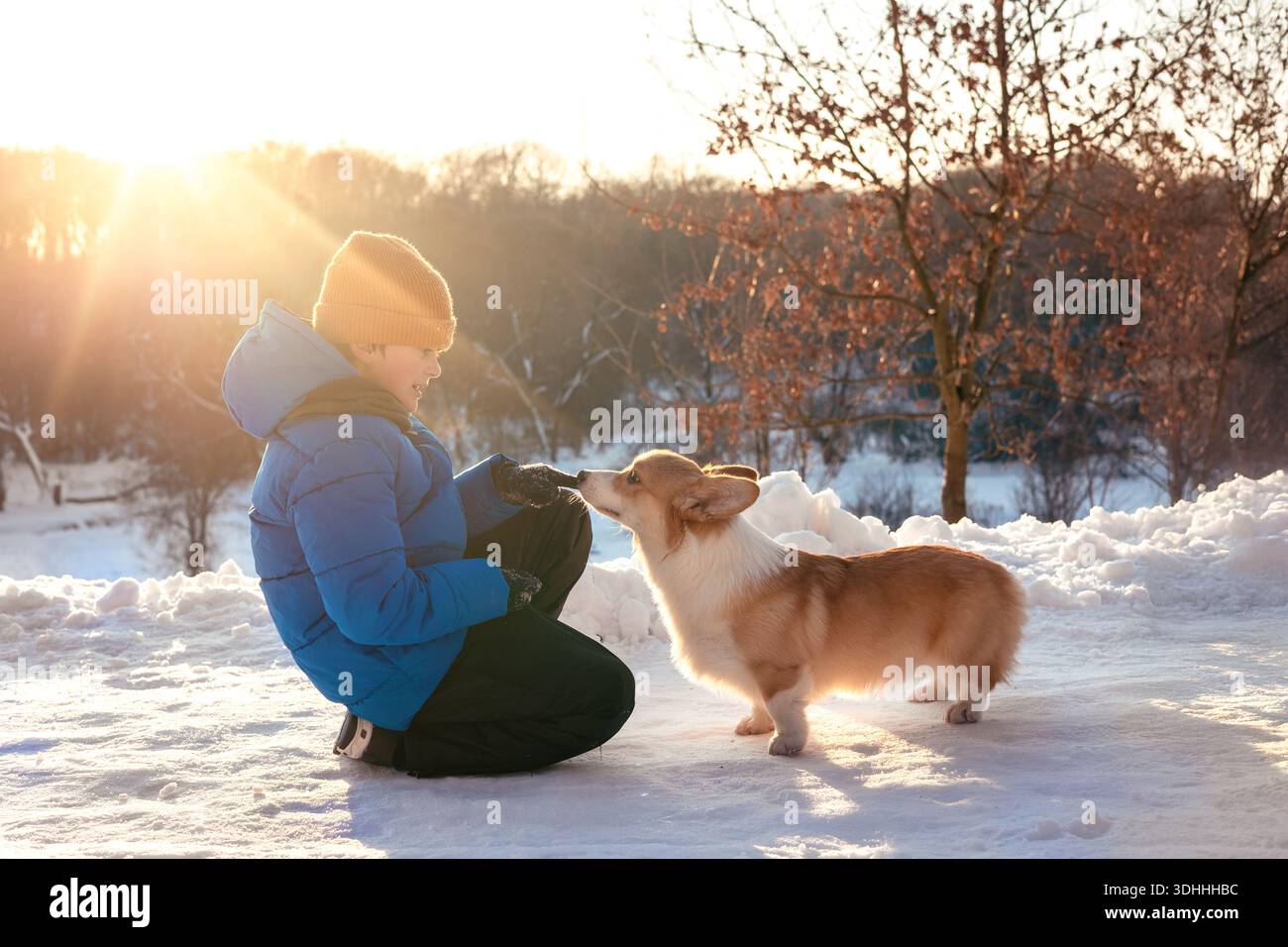 bambini che giocano con un cane corgi all'aperto durante l'inverno in un parco innevato. Calda interazione tra un bambino e un animale domestico. Infanzia, cura degli animali, amicizia Foto Stock