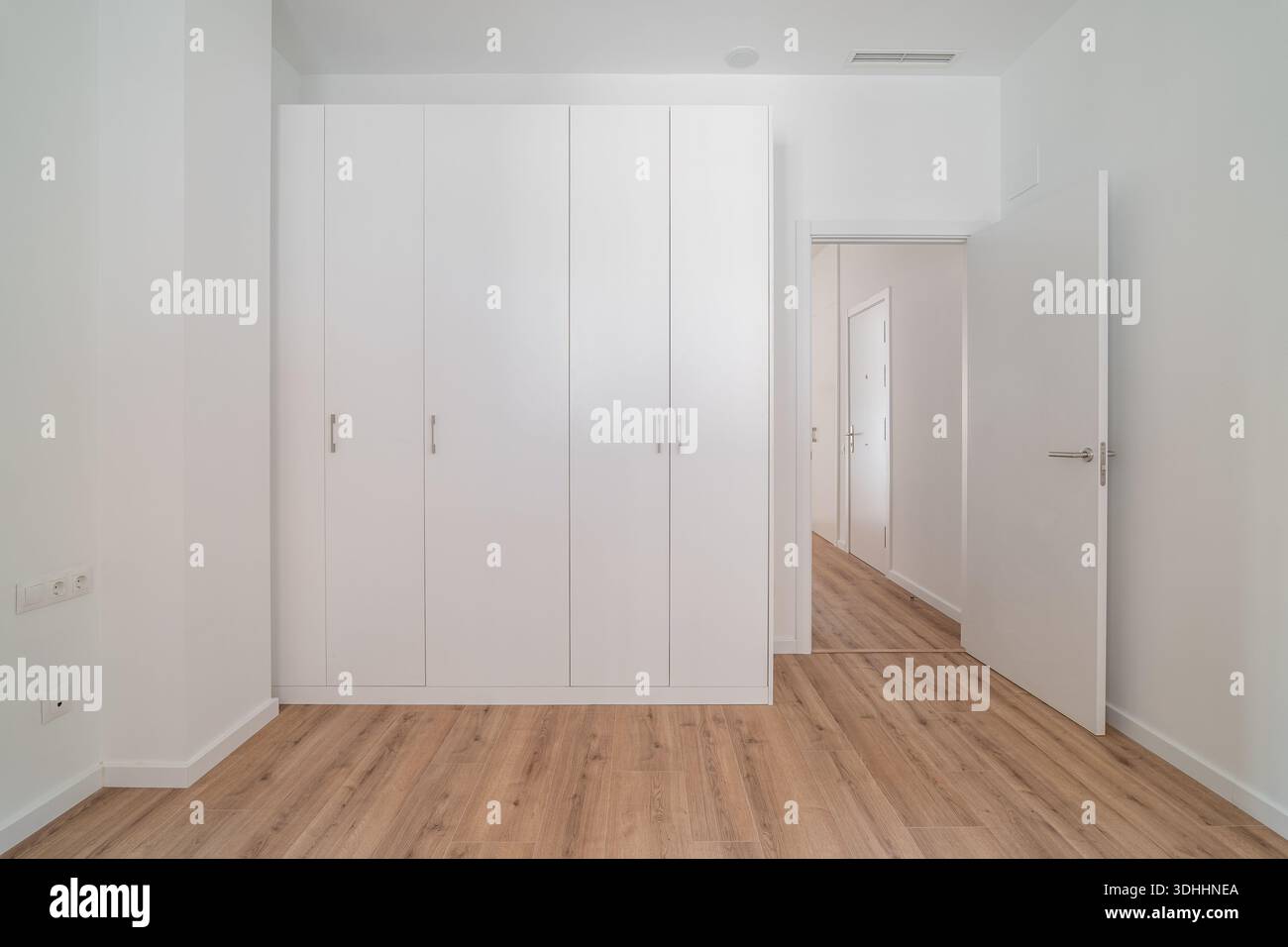 Un interno luminoso e minimalista caratterizzato da un armadio bianco e pavimento in legno. Le pareti sono semplici e lo spazio è ordinato, sottolineando la semplicità Foto Stock