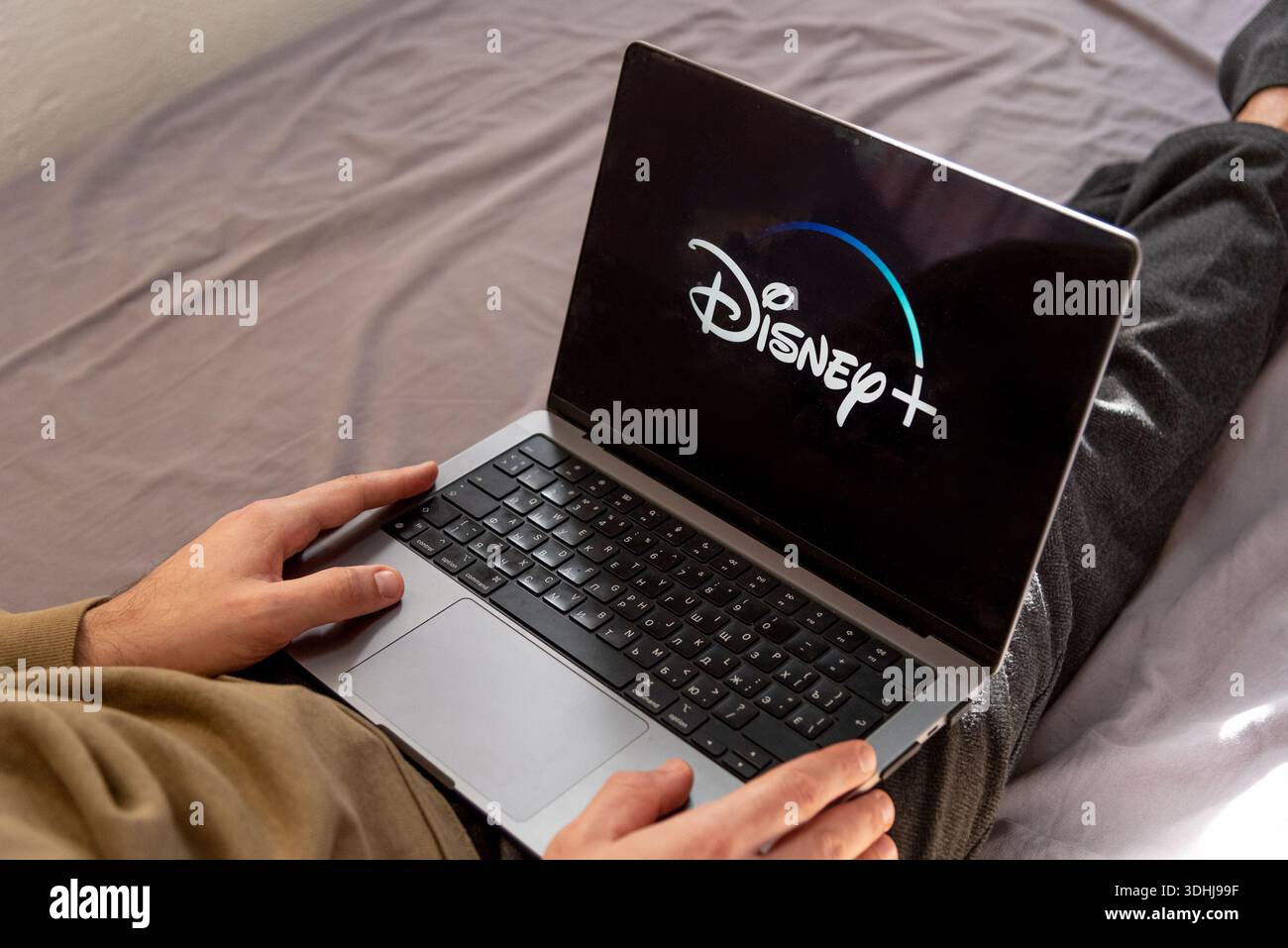 Uomo che guarda un film sulla piattaforma Disney Plus su un computer portatile seduto sul letto di casa Foto Stock