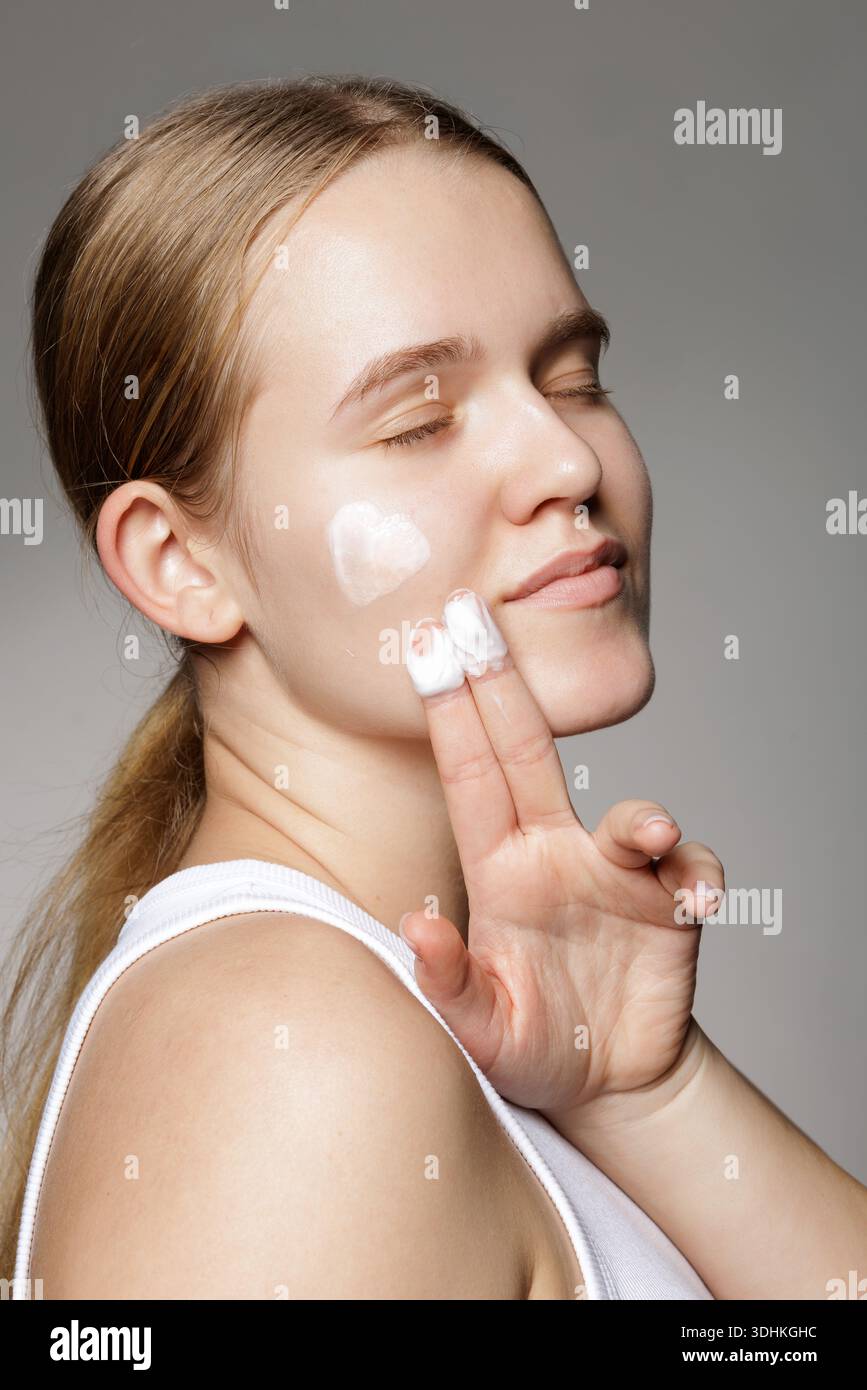 Ritratto in studio di una giovane donna che applica idratante per il viso su pelle con tendenza a difetti per banner di siti Web, blog per la cura della pelle o pubblicità sociale. Foto Stock