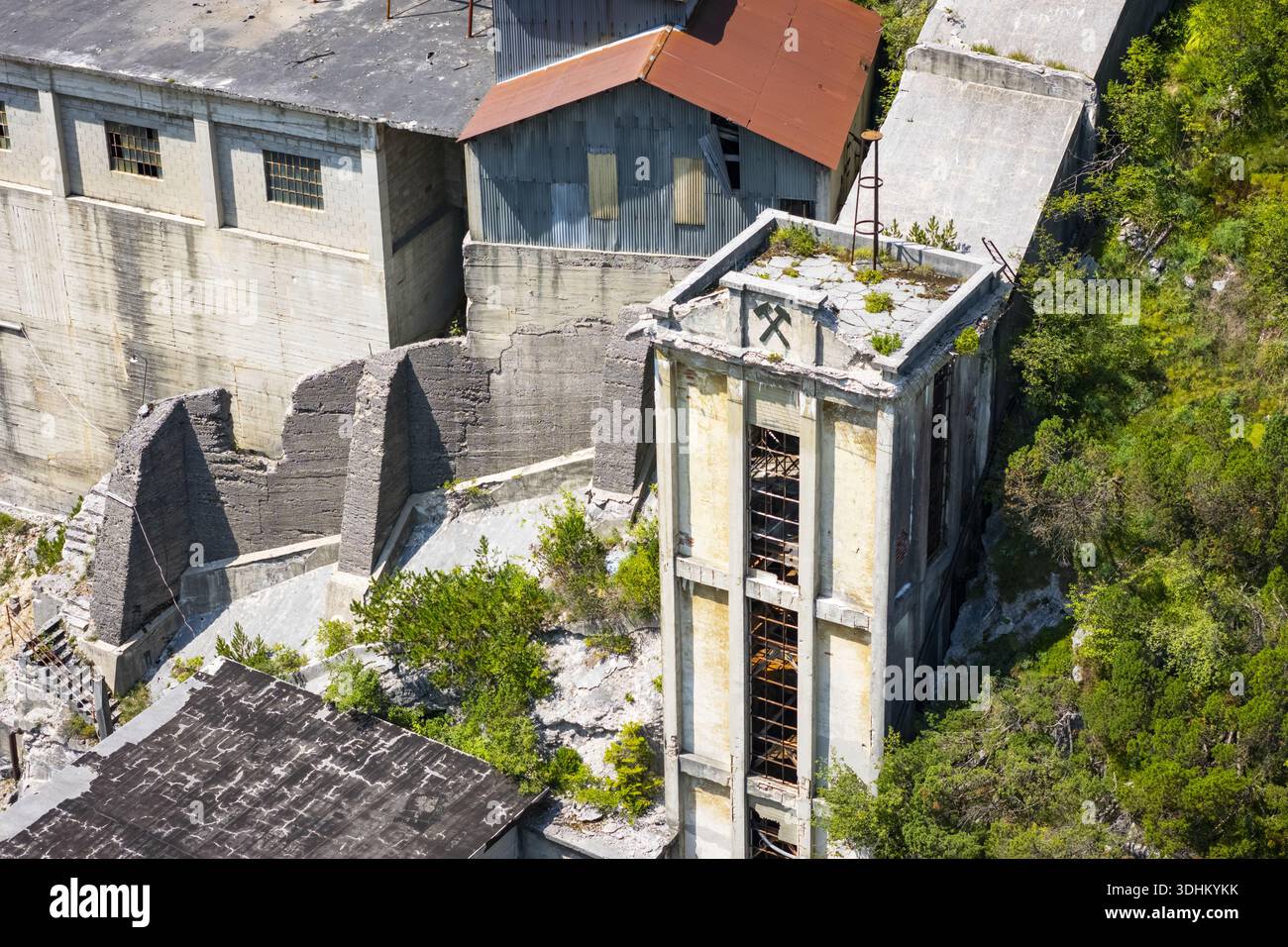 Veduta aerea degli edifici duri e intemprati della Cave del Predil si stagliano in silenzioso contrasto con il vivace fogliame verde, Rabelj, Friuli-Venezia Gi Foto Stock