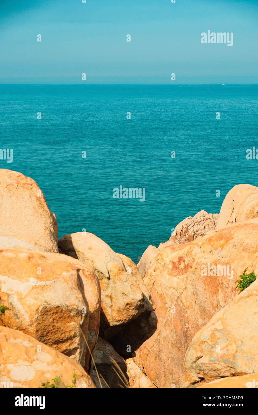 Scogliere costiere rocciose e piccoli isolotti lungo la costa, con mare turchese, rocce aspre, nebbia leggera su pendii boscosi Foto Stock