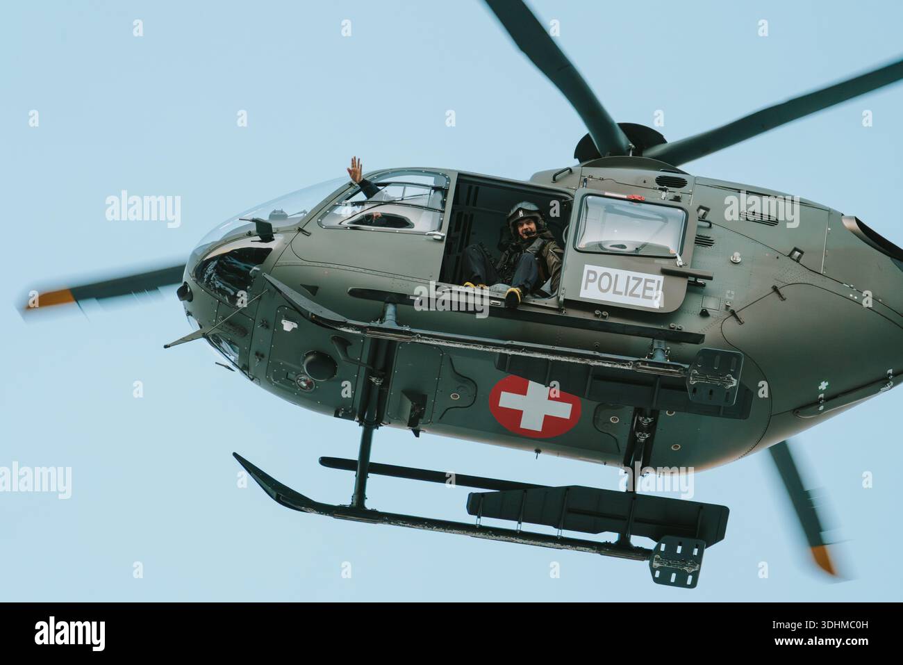 Elicottero della polizia svizzera in volo con un ufficiale che sventolava durante un'operazione di sicurezza Foto Stock