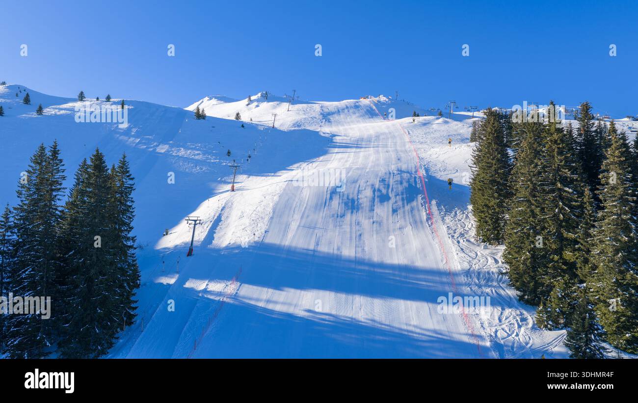 Ampia pista da sci ben curata che scende attraverso la foresta alpina, preparata per gli sport invernali, lo snowboard e il turismo di montagna stagionale Foto Stock