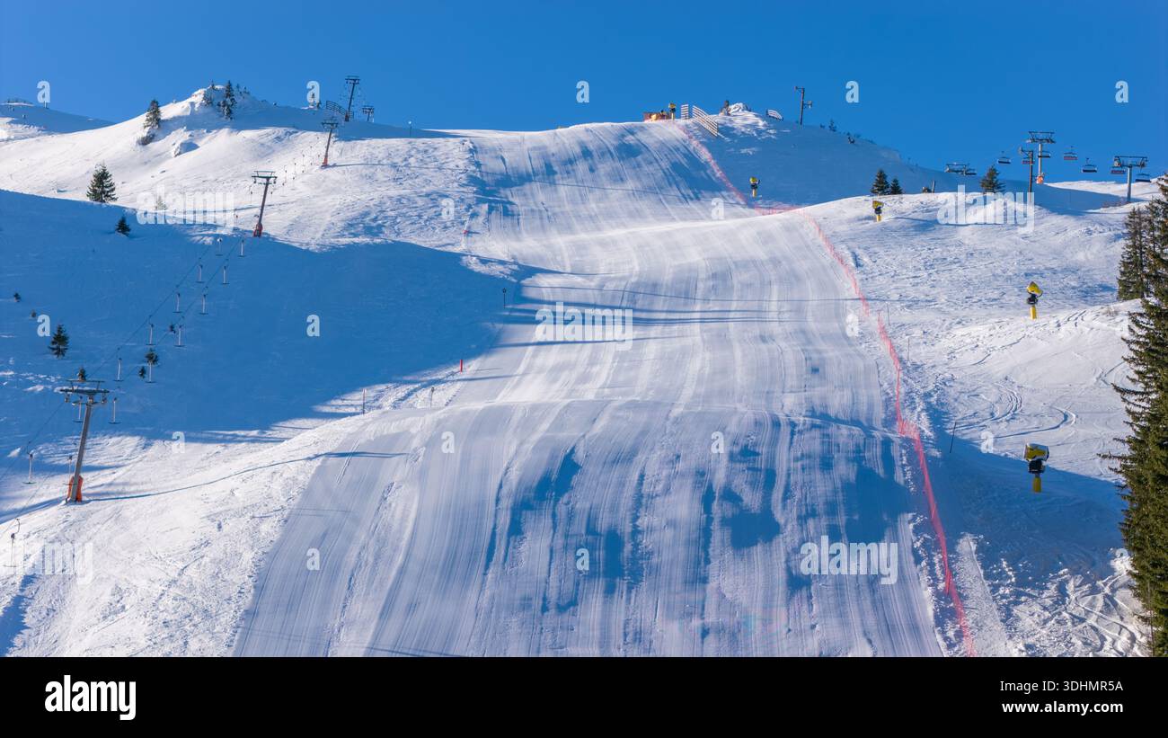 Pista da sci ripida e curata con struttura nevosa visibile e infrastrutture di risalita, catturata nelle brillanti condizioni invernali per gli sport alpini e la promozione del resort Foto Stock