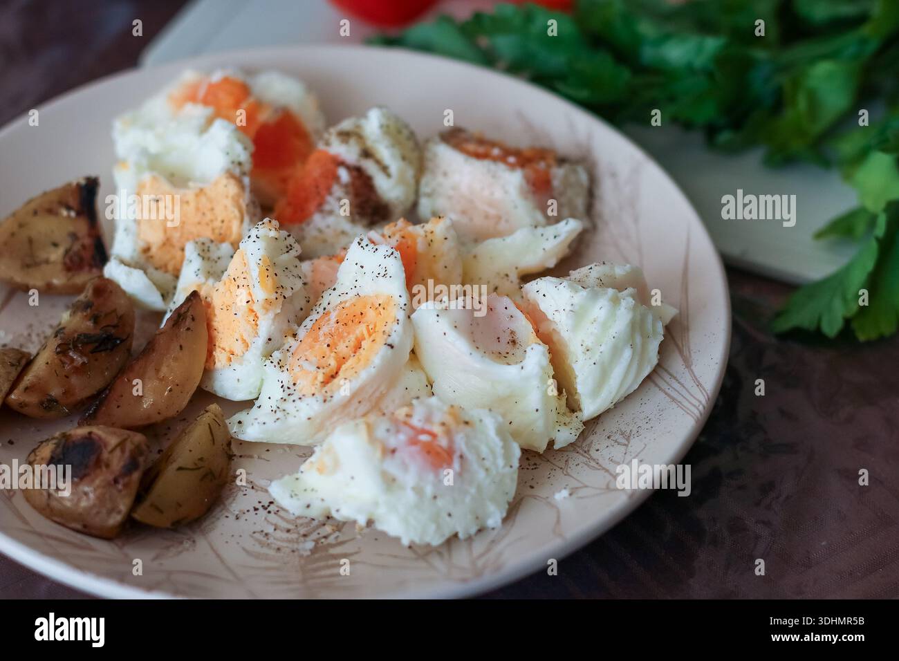 Shot intimo di piatto contenente uova, patate arrosto, funghi fritti, accanto a pomodori ed erbe a bordo Foto Stock