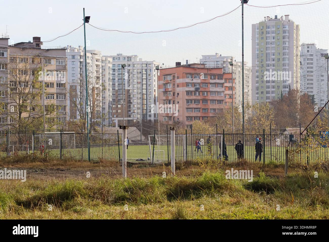 Persone impegnate in una partita di calcio informale su un campo erboso circondato da alte torri residenziali nel paesaggio urbano Foto Stock