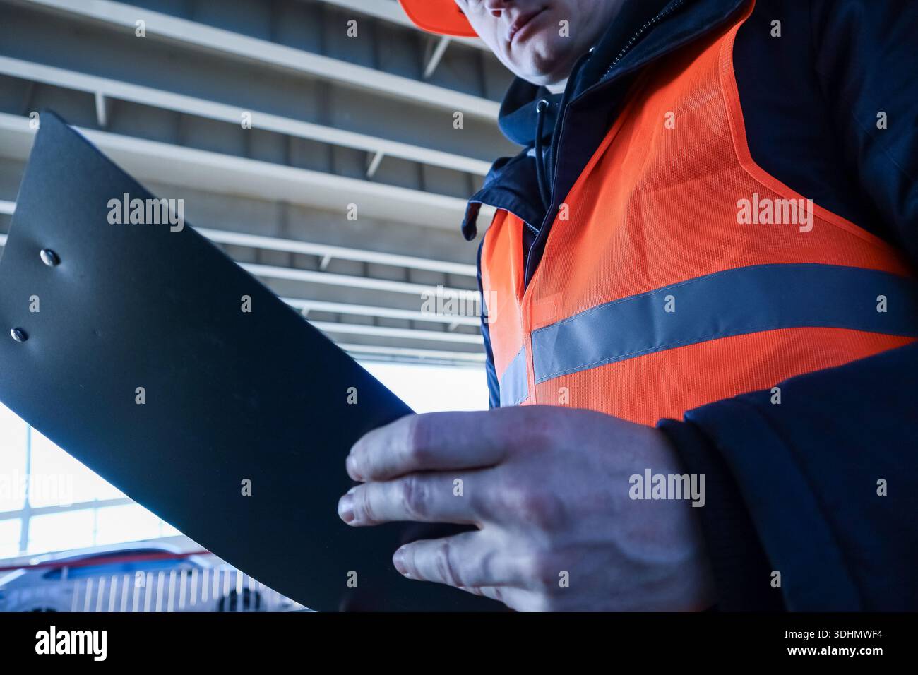 Primo piano estremo della mano maschile in un dispositivo di sicurezza che tiene il portadocumenti nero sotto la struttura del soffitto industriale. Foto Stock