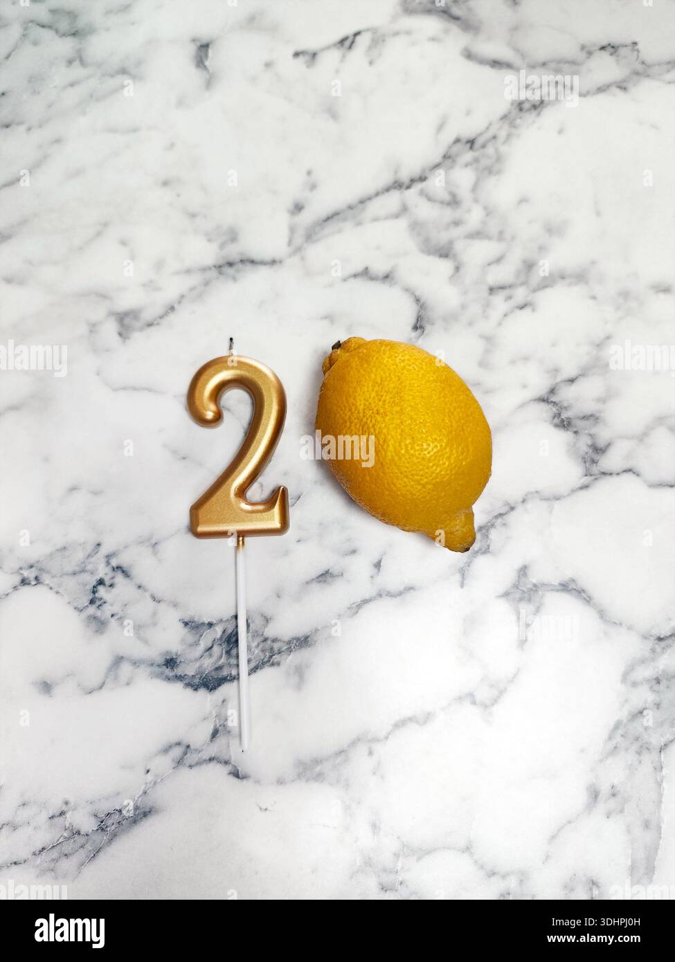 Sulla superficie di marmo si trovano una candela dorata a forma di numero 2 e un limone. composizione, 2 milioni, blogger, festeggiamenti, abbonati Foto Stock