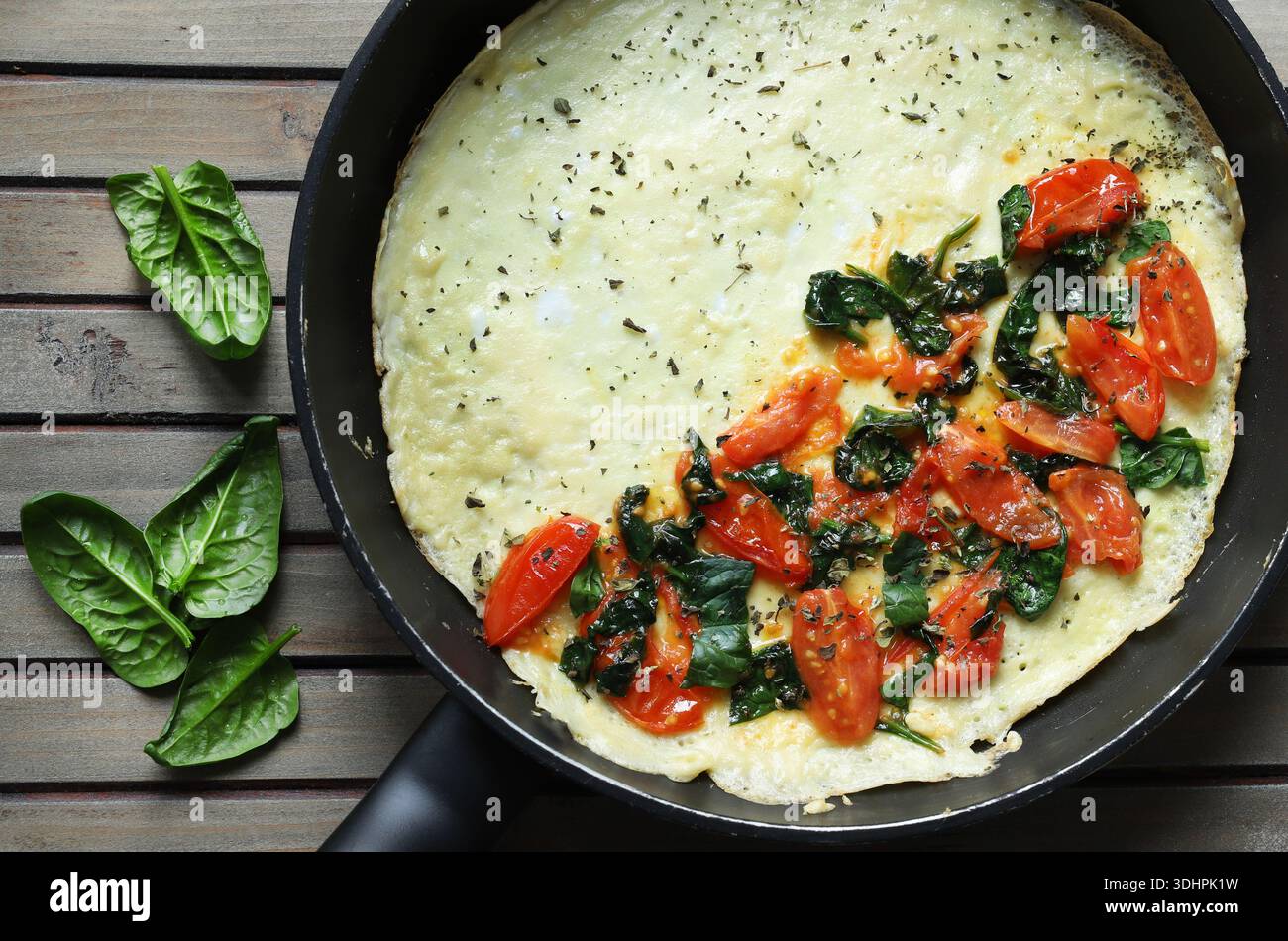 Una salata frittata o frittata con spinaci freschi e pomodori ciliegini in una padella. Sfondo in legno. Vista dall'alto. Foto Stock