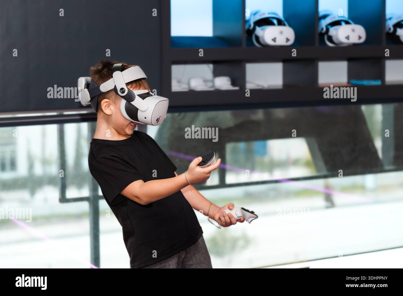 Il bambino gioca con occhiali VR e controller in un moderno showroom durante il giorno, mostrando la tecnologia della realtà virtuale Foto Stock