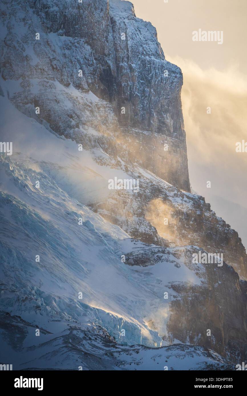 Vista di una maestosa parete di montagna con neve e neve che soffia catturando la luce dorata del sole, Improvement District No. 9, Canada. Foto Stock