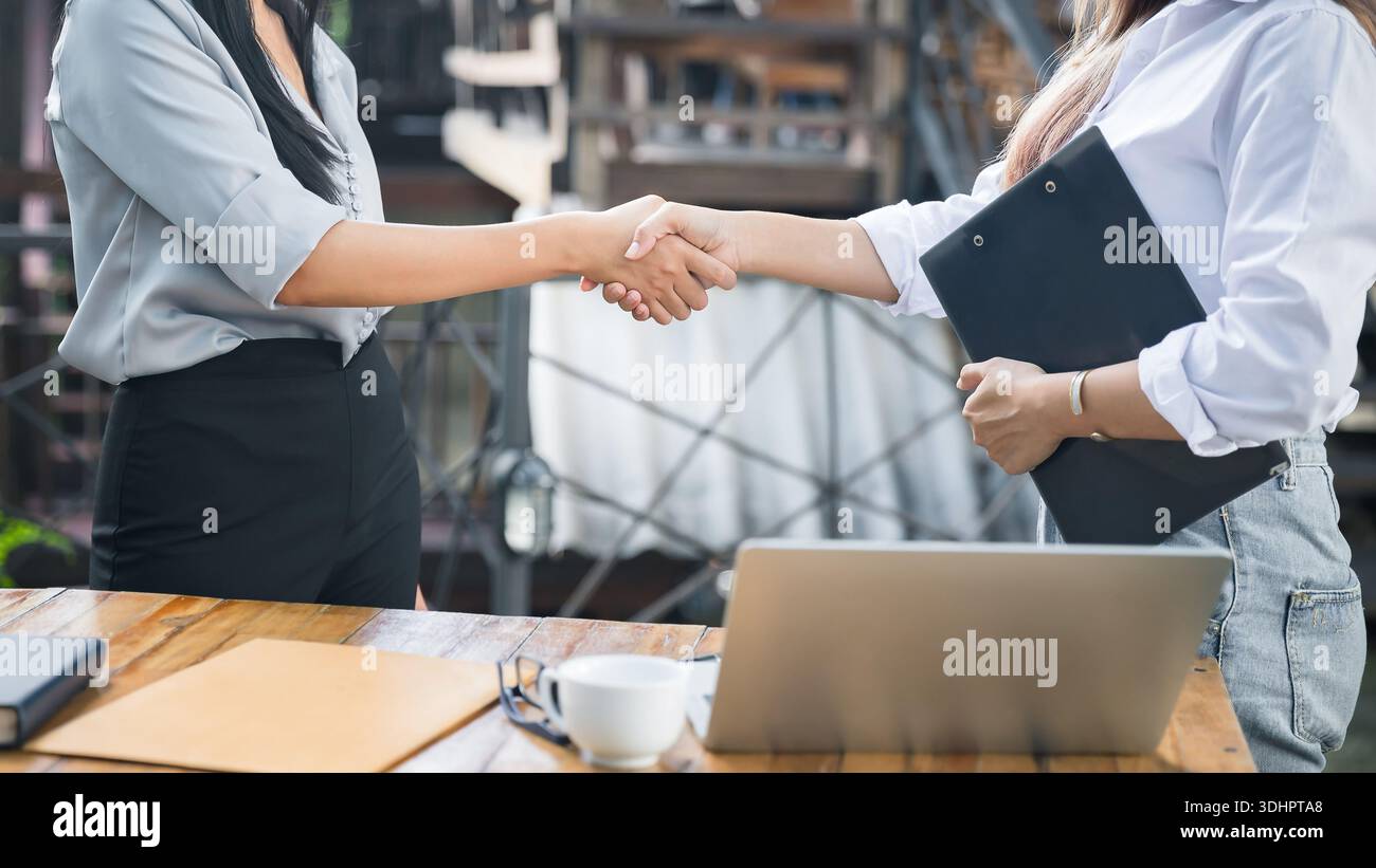 Due donne asiatiche architetto e ingegnere in caschi protettivi tremano la mano dopo l'incontro. Concetto di collaborazione di successo. Foto Stock
