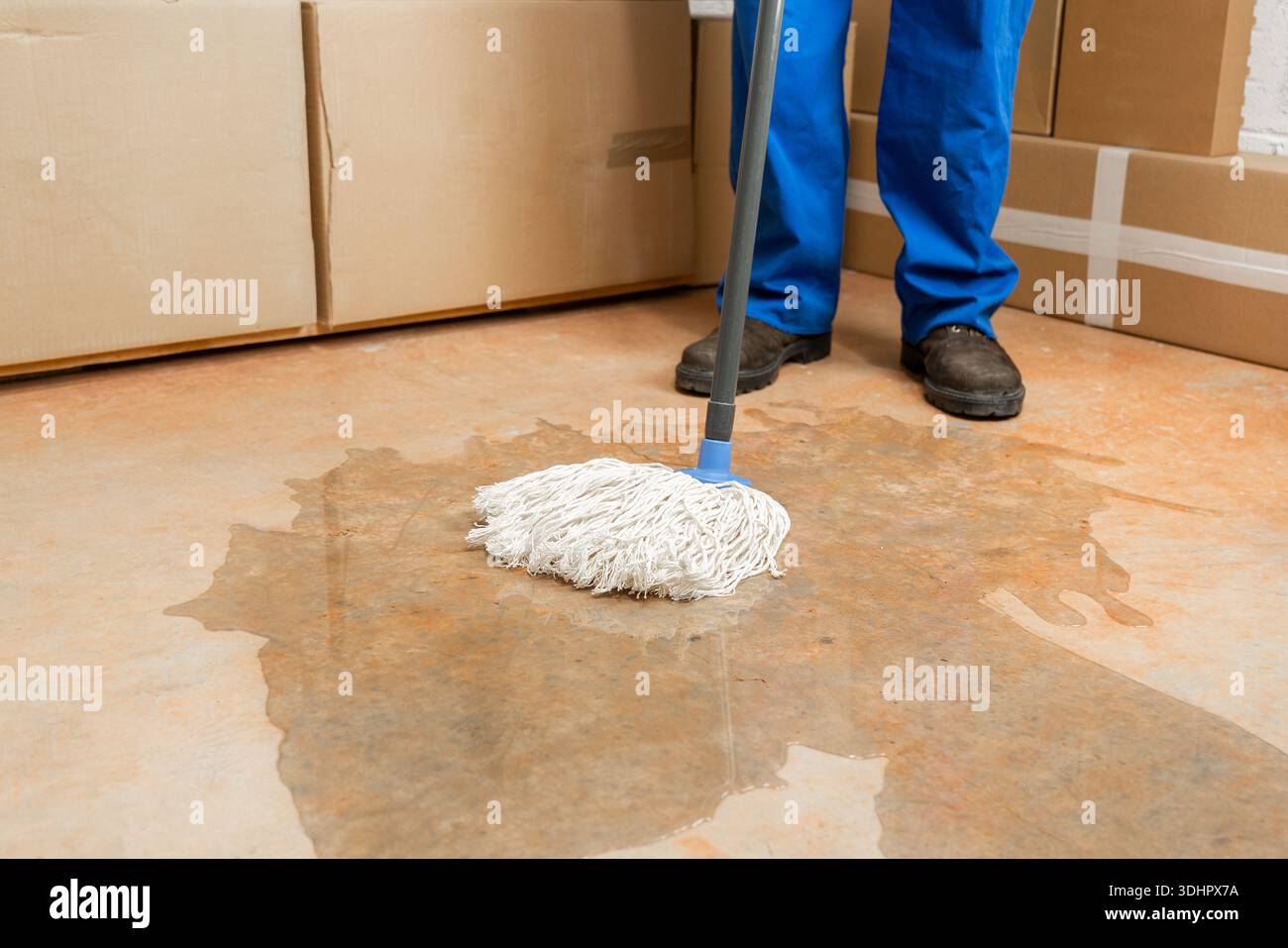 Lavoratore maschile che pulisce un pericolo di scivolamento sul pavimento di un impianto industriale con mocio bianco. Foto Stock
