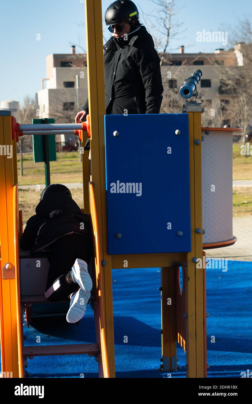 Bambini che strisciano in un parco giochi colorato mentre un adulto guarda nelle vicinanze Foto Stock
